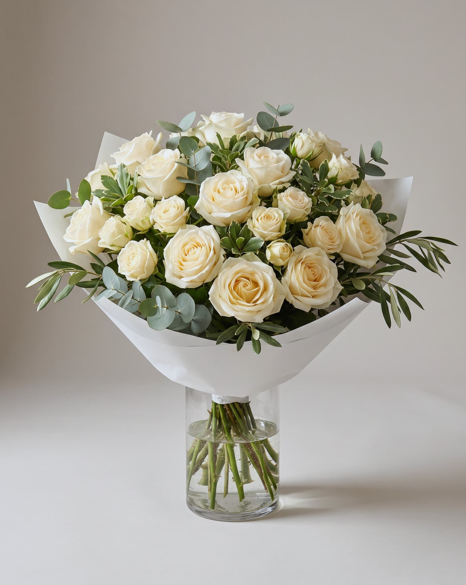 Cream roses with eucalyptus wrapped in white paper in a clear glass vase