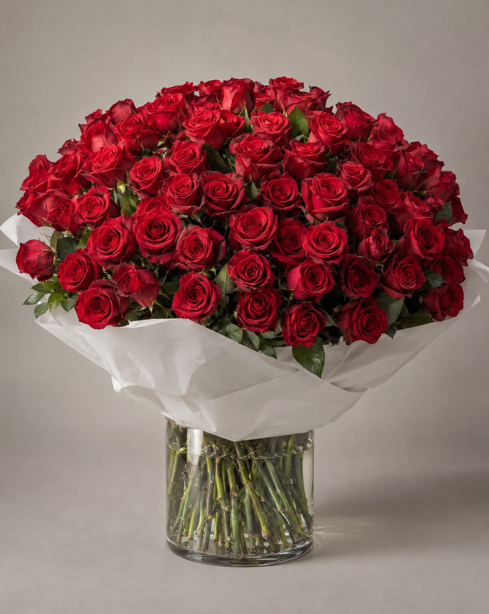 Red roses wrapped in white tissue in a clear glass vase