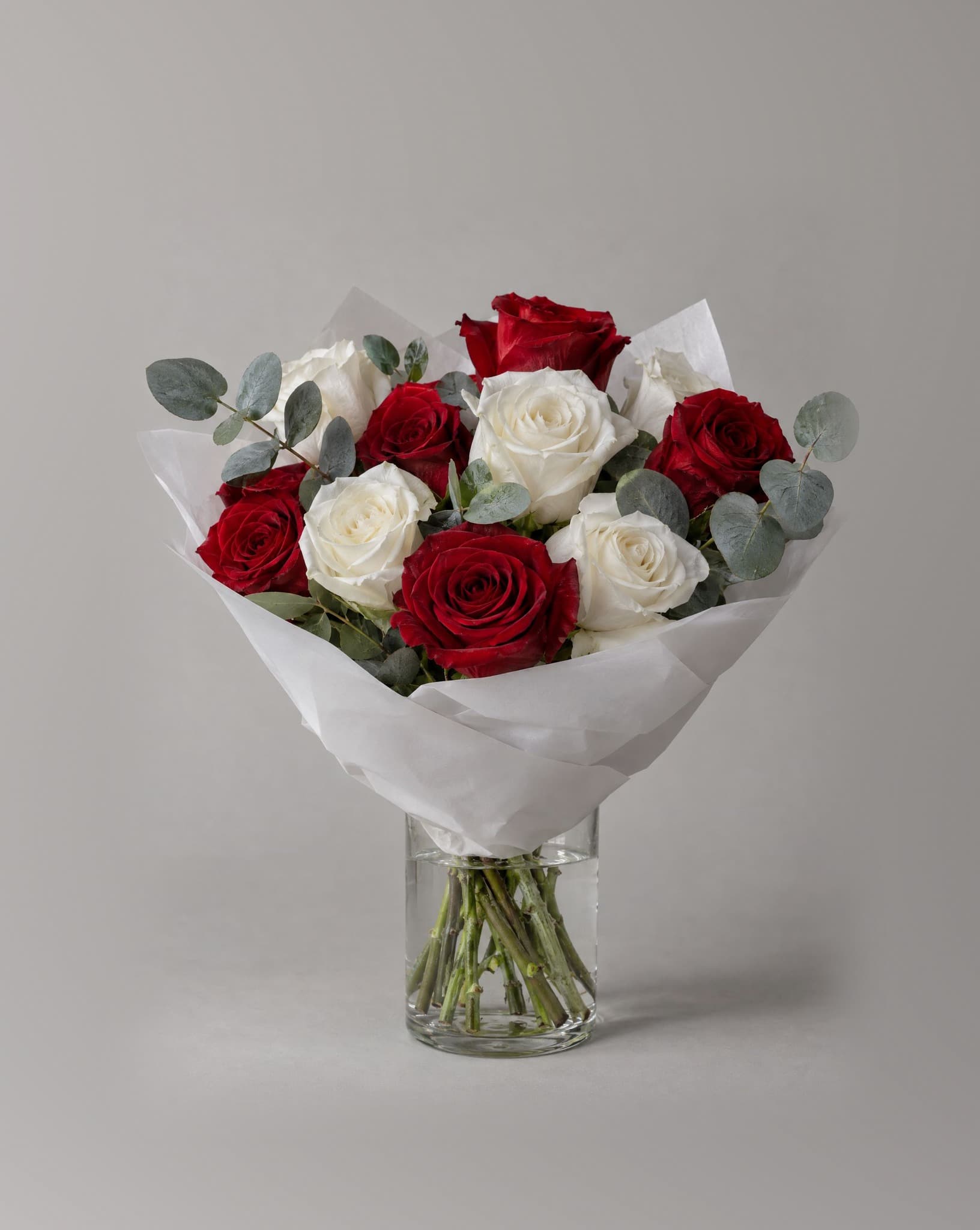 A dozen red and white roses with eucalyptus wrapped in white paper in a clear glass vase