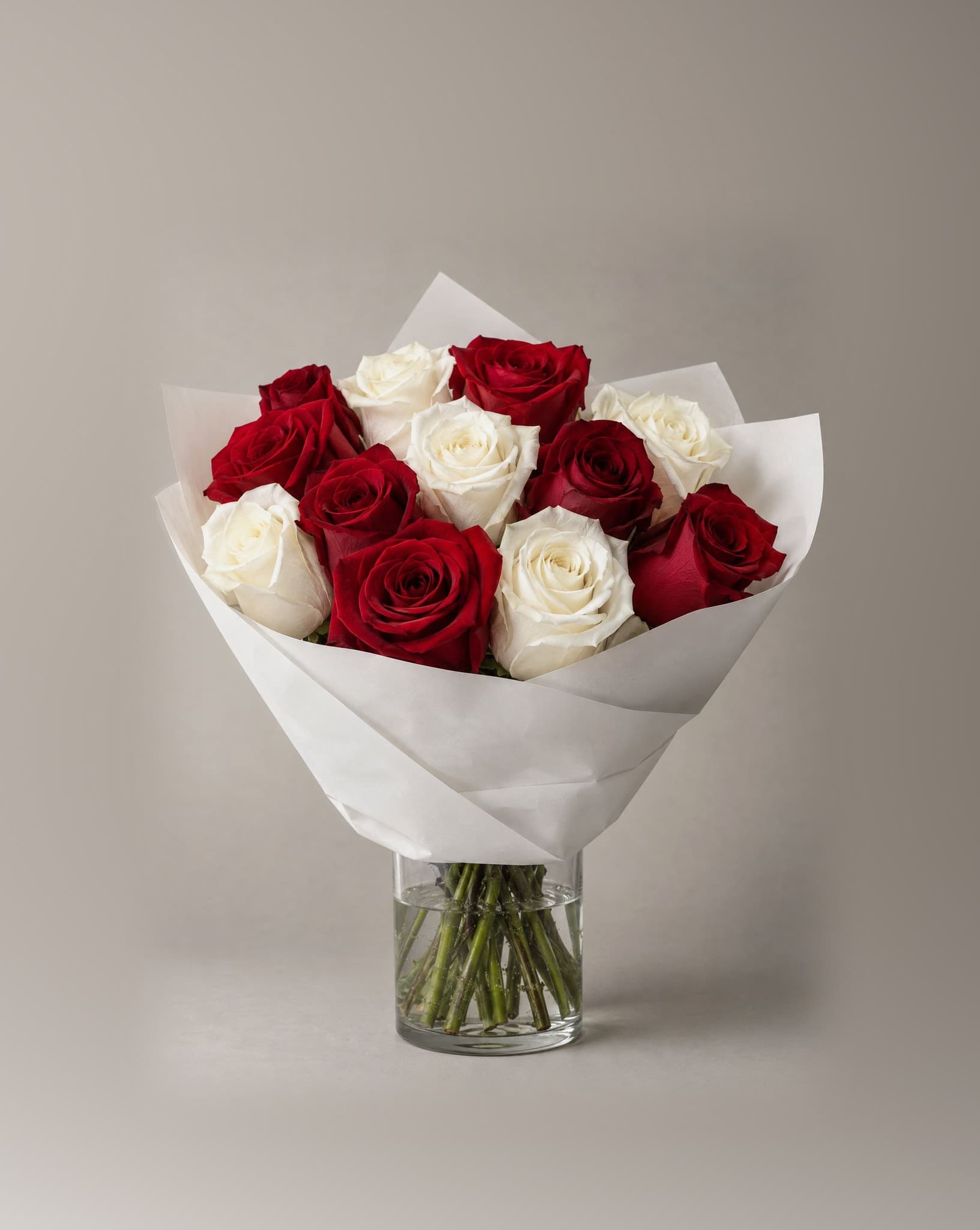 A dozen red and white roses wrapped in white paper in a clear glass vase