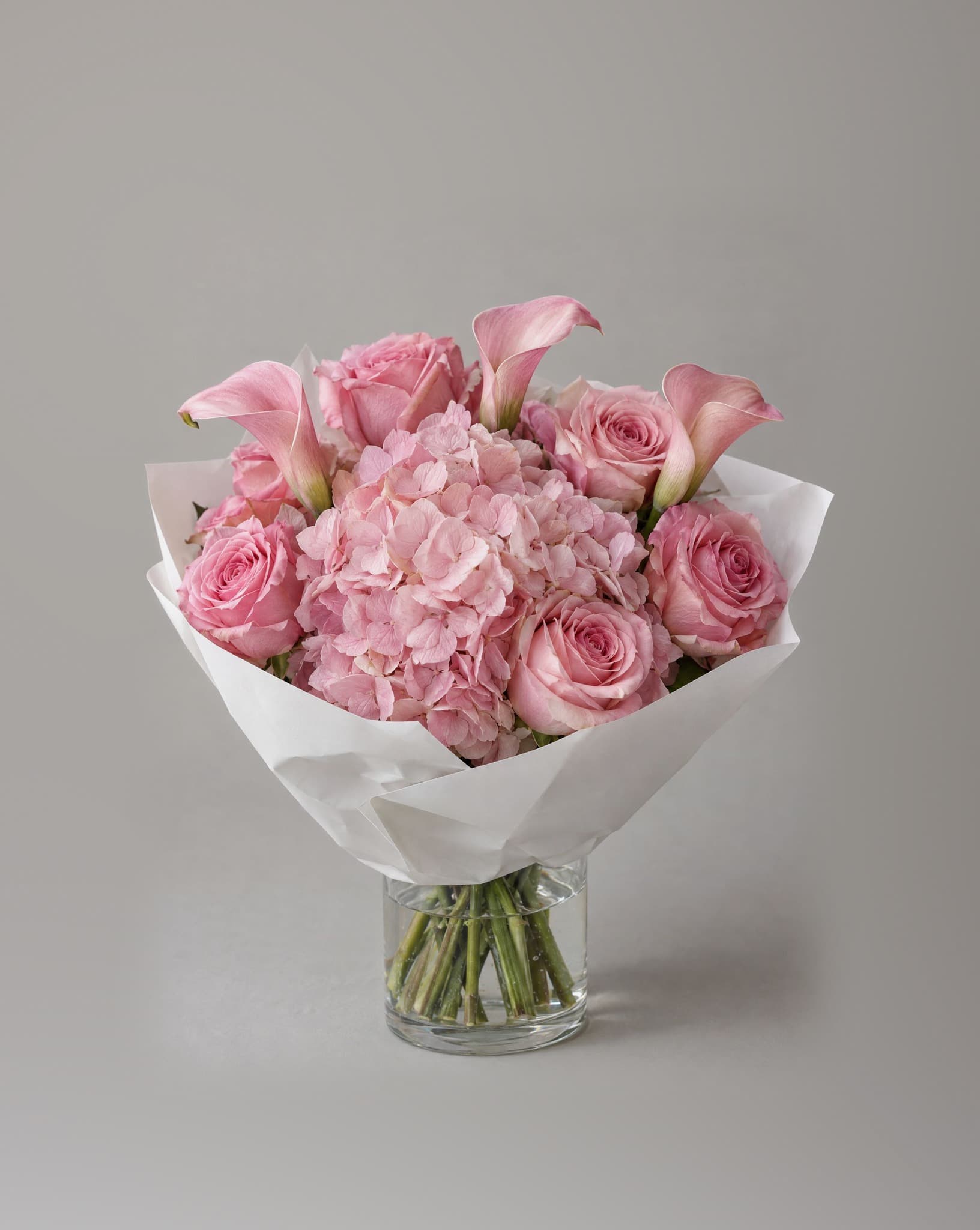 Standard bouquet of pink hydrangeas, pink roses and blush calla lilies in a clear glass vase